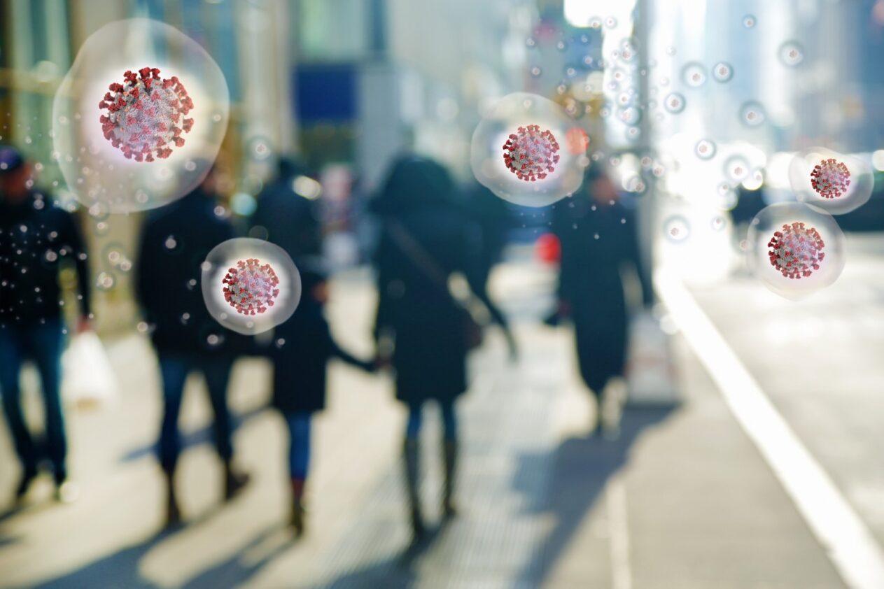 silhouetted people walking on a city street with five red circular virus particles representing COVID on top of them